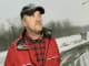 Man in red jacket and plaid shirt wearing a baseball cap, looking to the side.