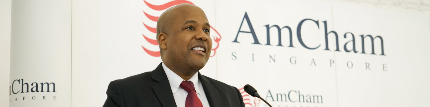 Man in suit speaking at podium with AmCham Singapore logo