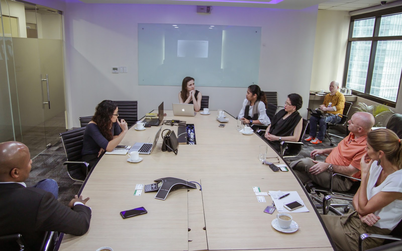 People in a boardroom meeting with laptops and papers on a large table.