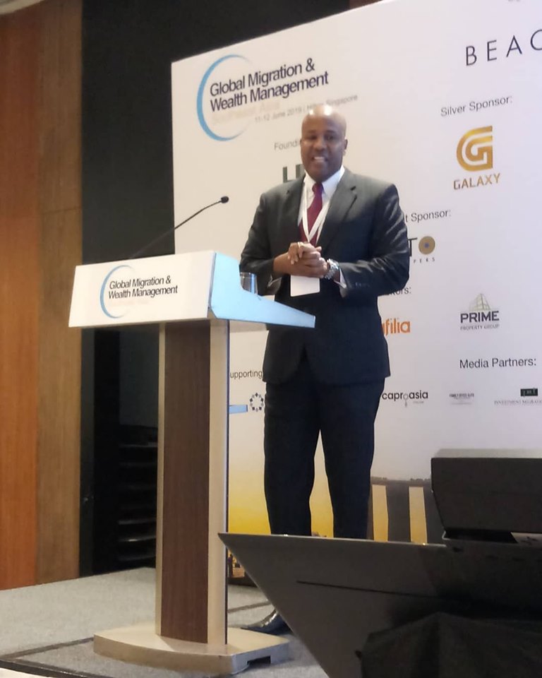 Man in suit at podium for Global Migration & Wealth Management event in Singapore.