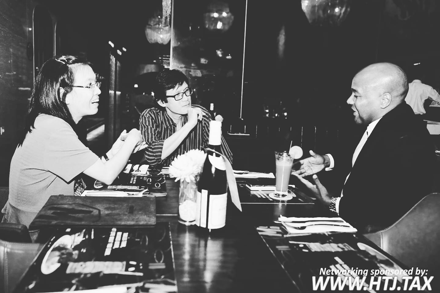 Three people talking at a table with drinks and a bottle of wine.