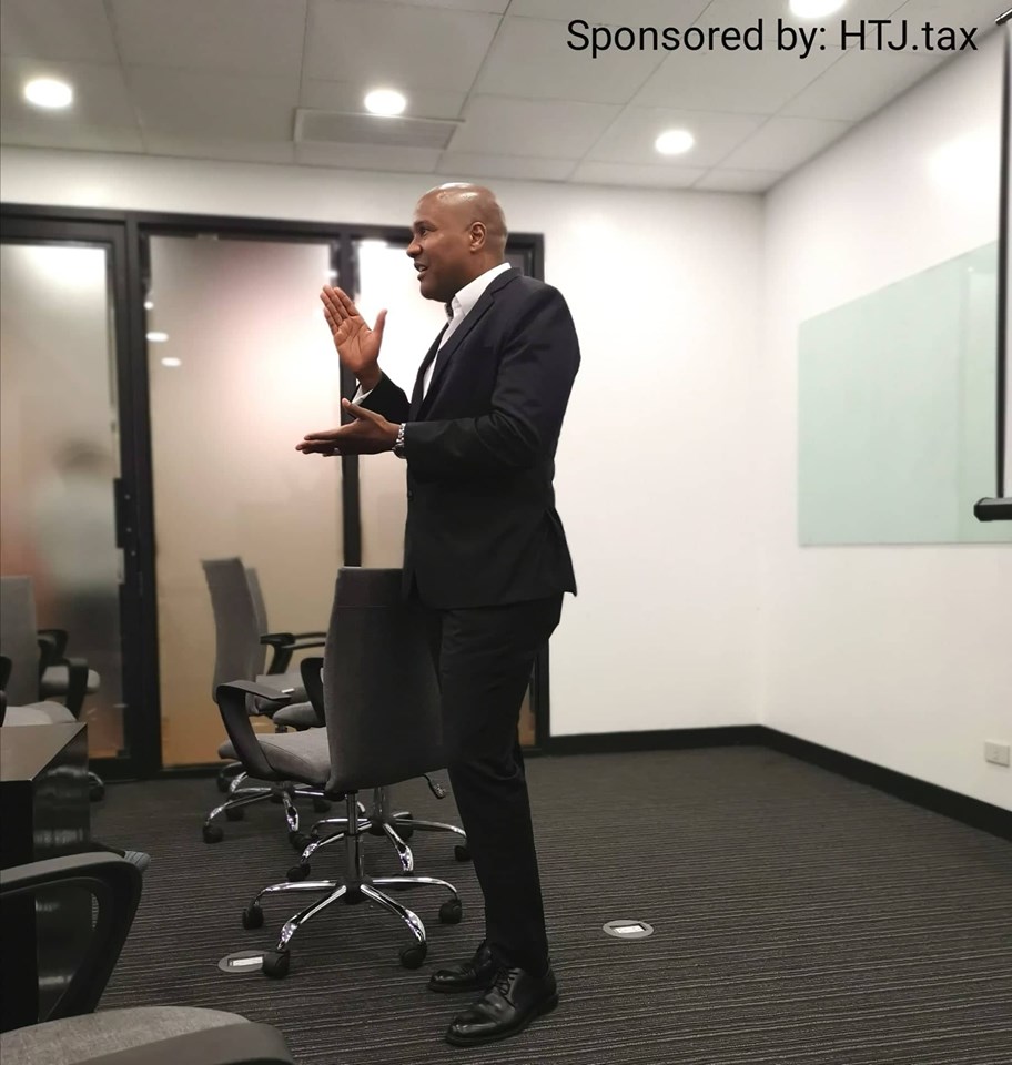 Man in a suit gesturing in a conference room. Sponsored by HTJ.tax.