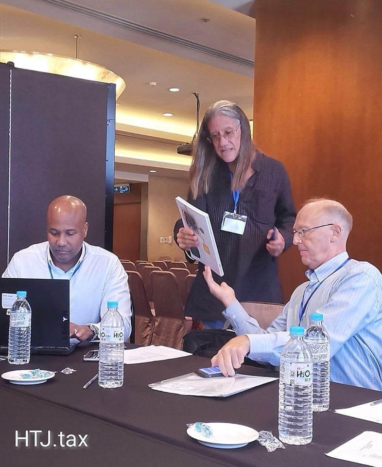 Three people at a table during a presentation, one holding a booklet.