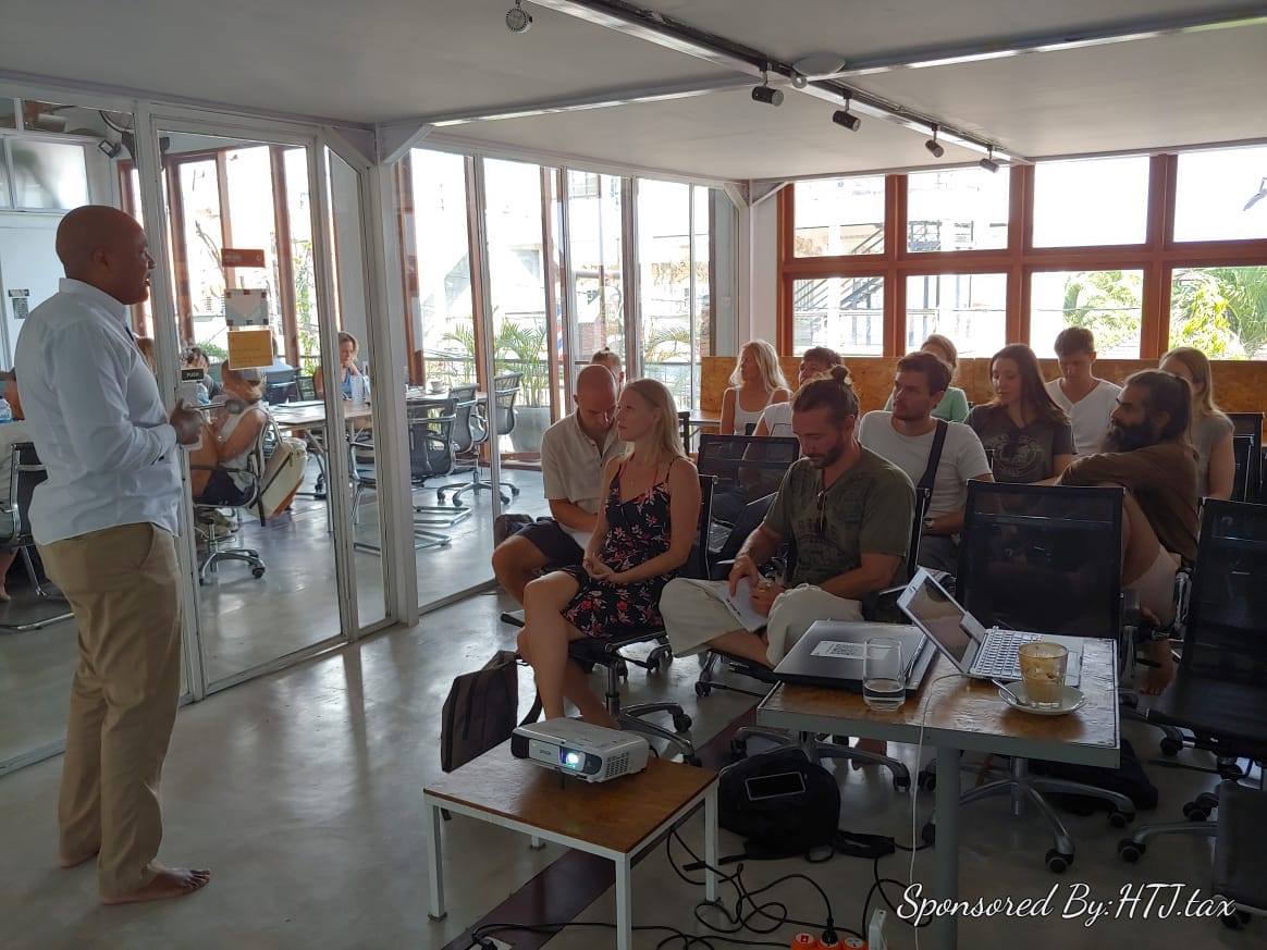 Man in white shirt presents to seated audience in modern office space.