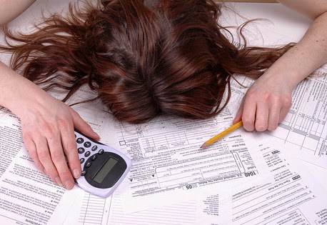 Person with head down on tax forms, holding calculator and pencil.