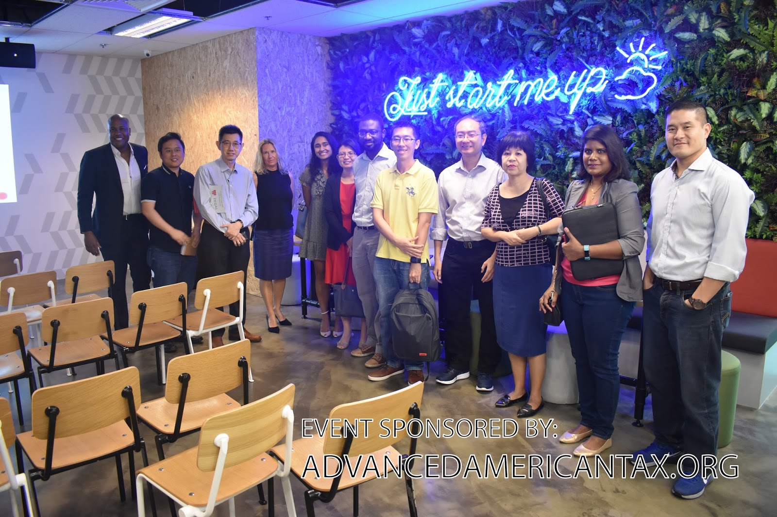 Group of people standing in front of a wall with a neon sign and plants. Text overlay reads "EVENT SPONSORED BY