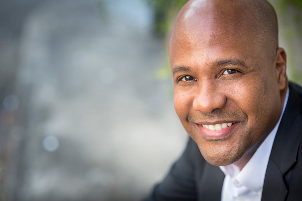 Derren Joseph smiles, wearing a suit and white shirt.