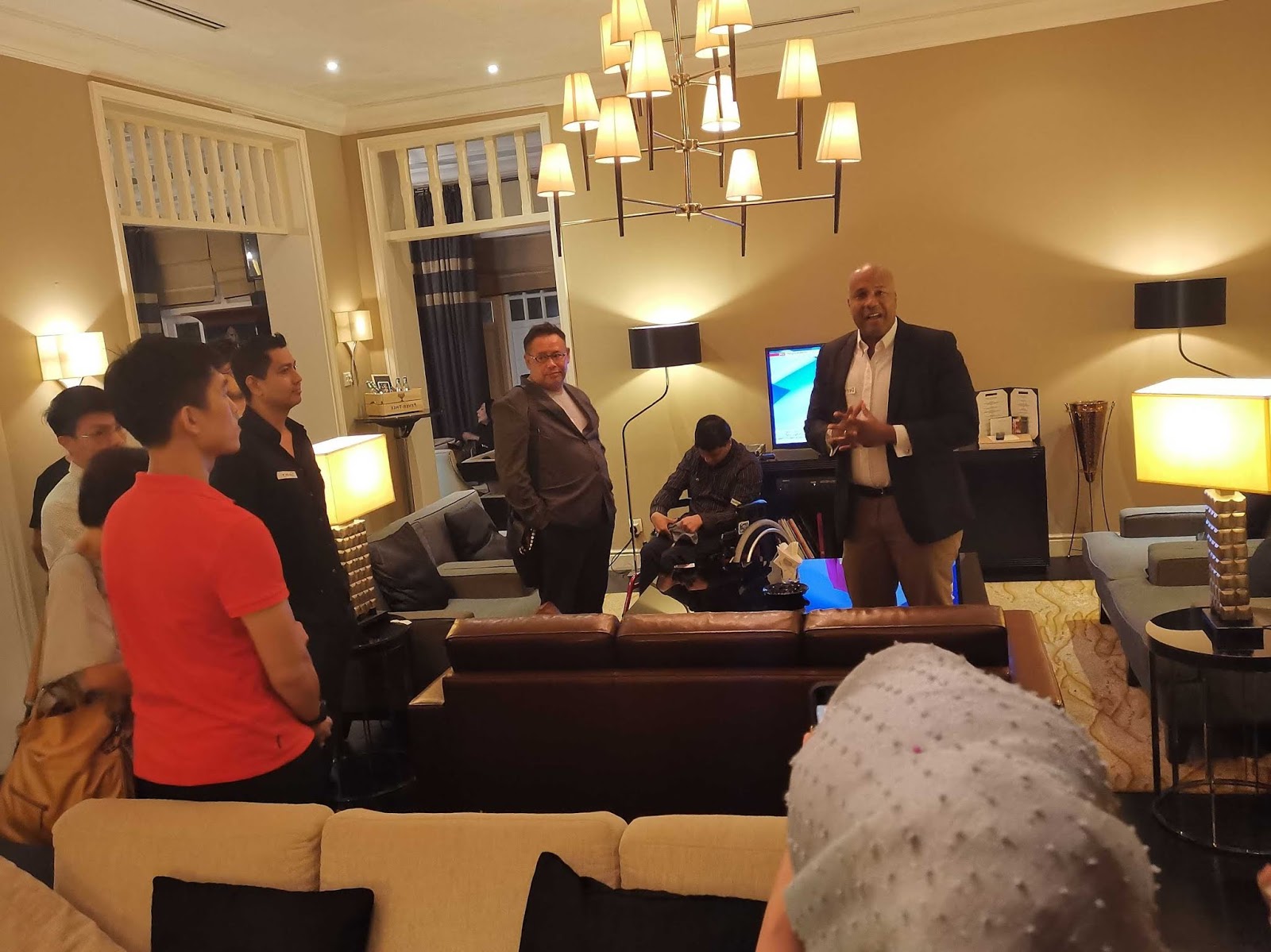 Man in suit speaking to a group of people in a lounge area.