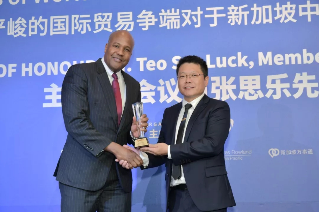 Two men in suits shaking hands, one receiving a trophy.