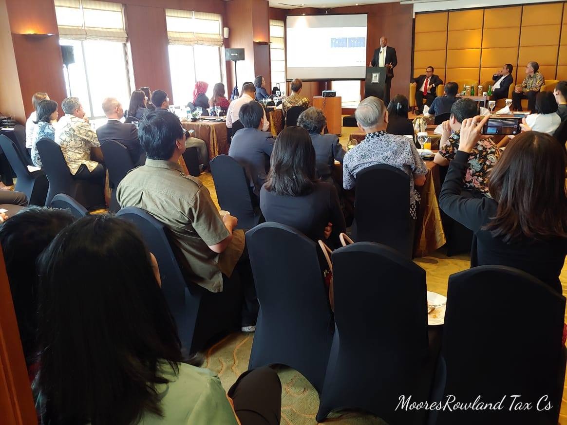 Speaker at podium presenting to an audience seated in chairs.