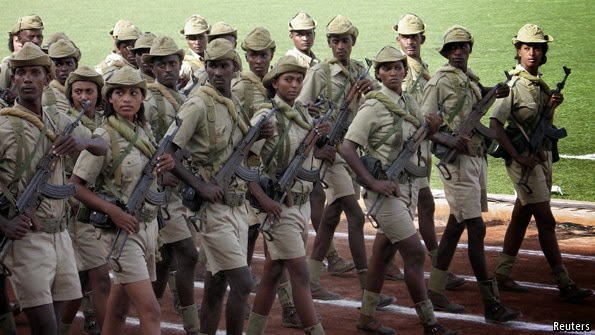Soldiers in tan uniforms and hats march with rifles on a track.