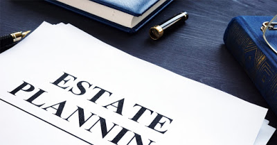 Paper with "ESTATE PLANNING" text, pen, and books on a dark surface.