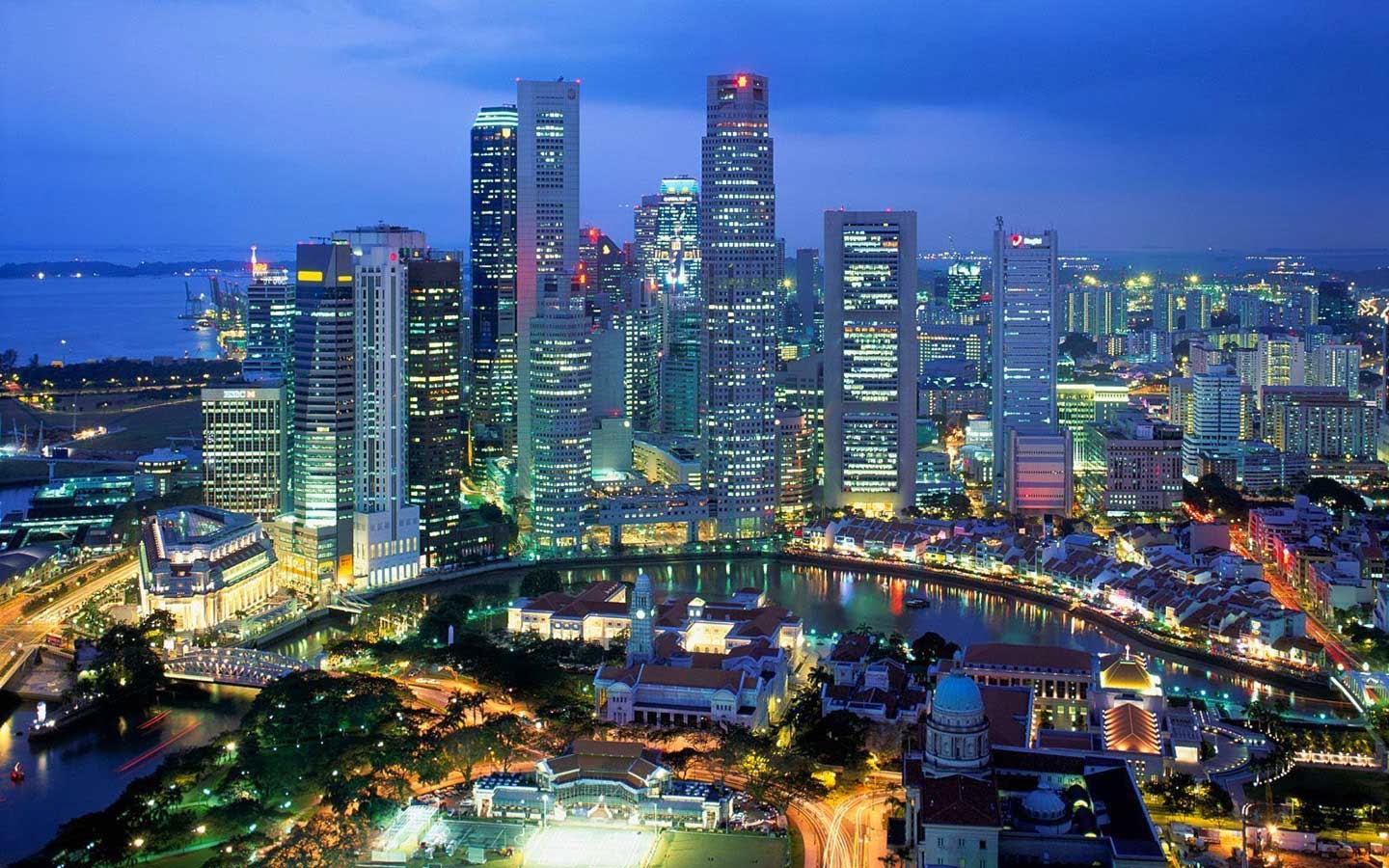 Singapore skyline at dusk with illuminated skyscrapers and a river.