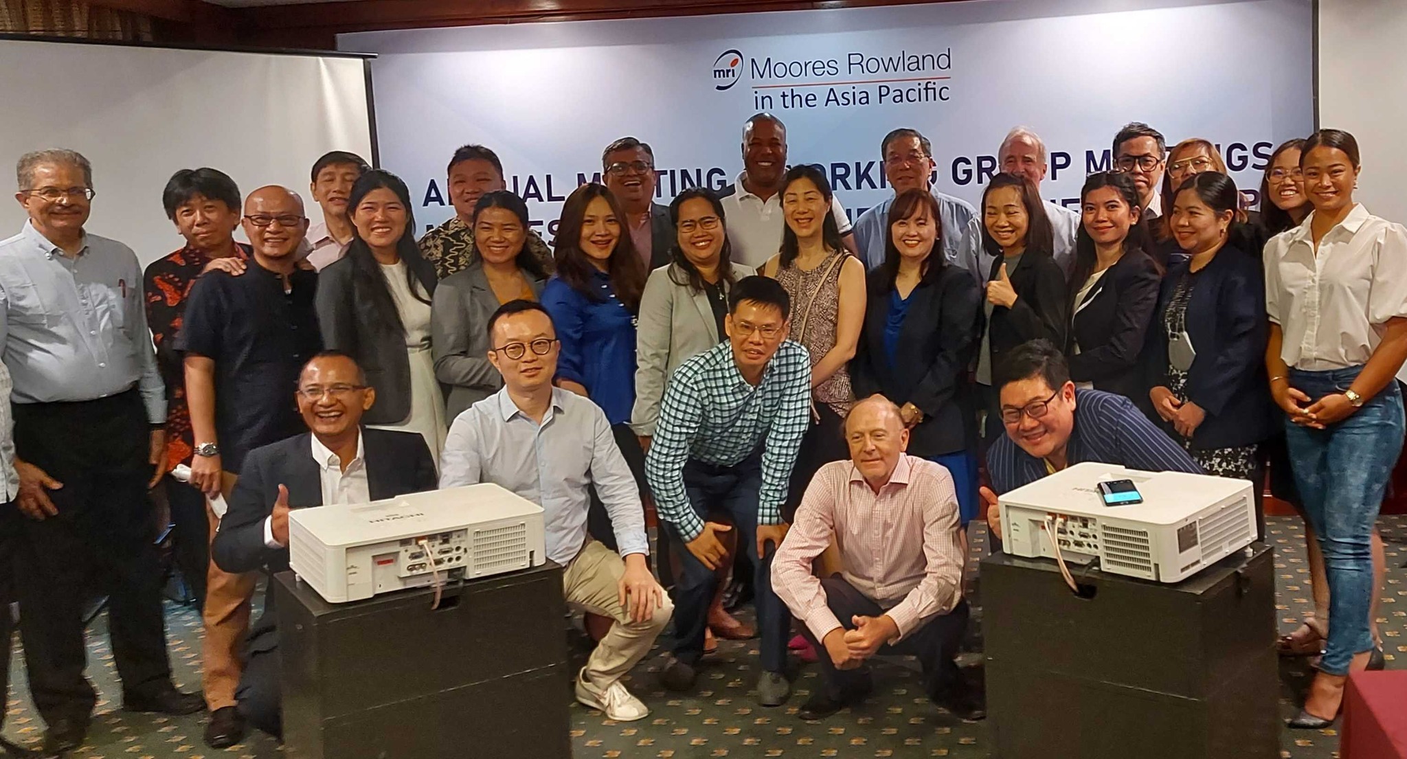 Moores Rowland Asia Pacific annual meeting group photo with attendees and projectors.